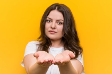 Young curvy plus size woman holding something with palms, offering to camera.