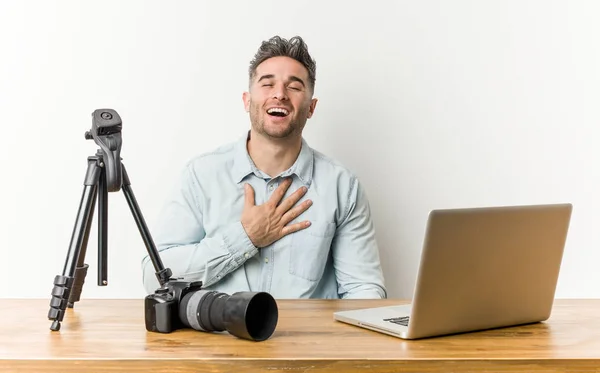Young handsome photography teacher laughs out loudly keeping hand on chest.