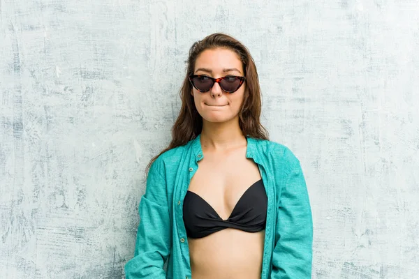 Young european woman wearing bikini confused, feels doubtful and unsure.