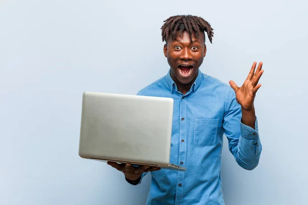Young rasta black man holding a laptop celebrating a victory or success