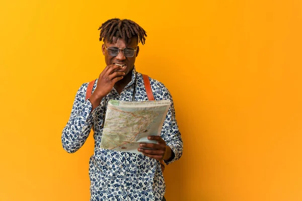 Young rasta black man holding a map biting fingernails, nervous and very anxious.
