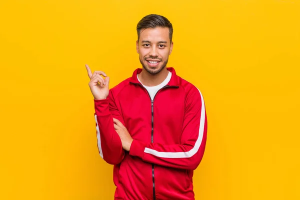Young filipino fitness man smiling cheerfully pointing with forefinger away.