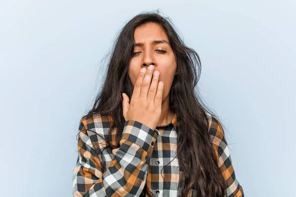 Young cool indian woman yawning showing a tired gesture covering mouth with him hand.