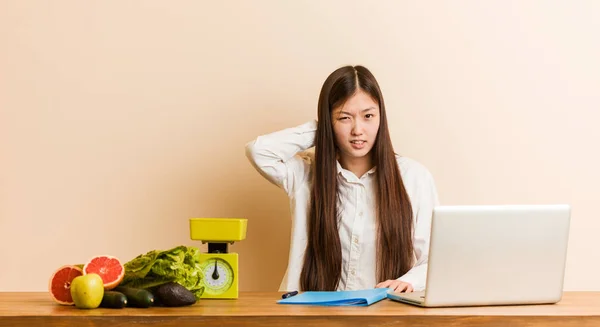 Young nutritionist chinese woman working with her laptop suffering neck pain due to sedentary lifestyle.