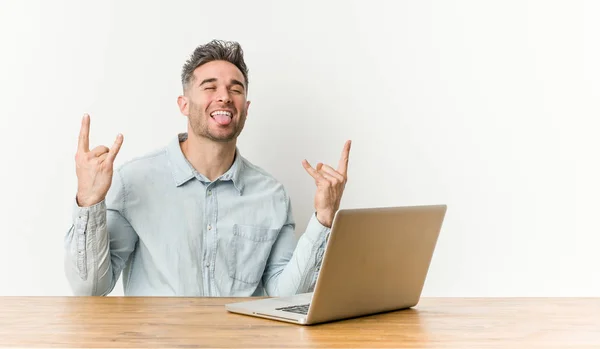 Jovem Homem Bonito Trabalhando Com Seu Laptop Mostrando Gesto Rocha — Fotografia de Stock