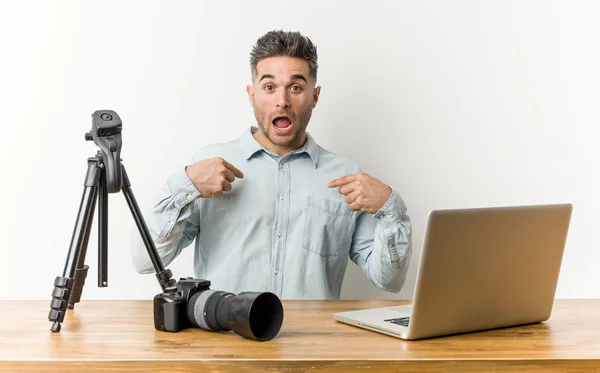 Young handsome photography teacher surprised pointing with finger, smiling broadly.