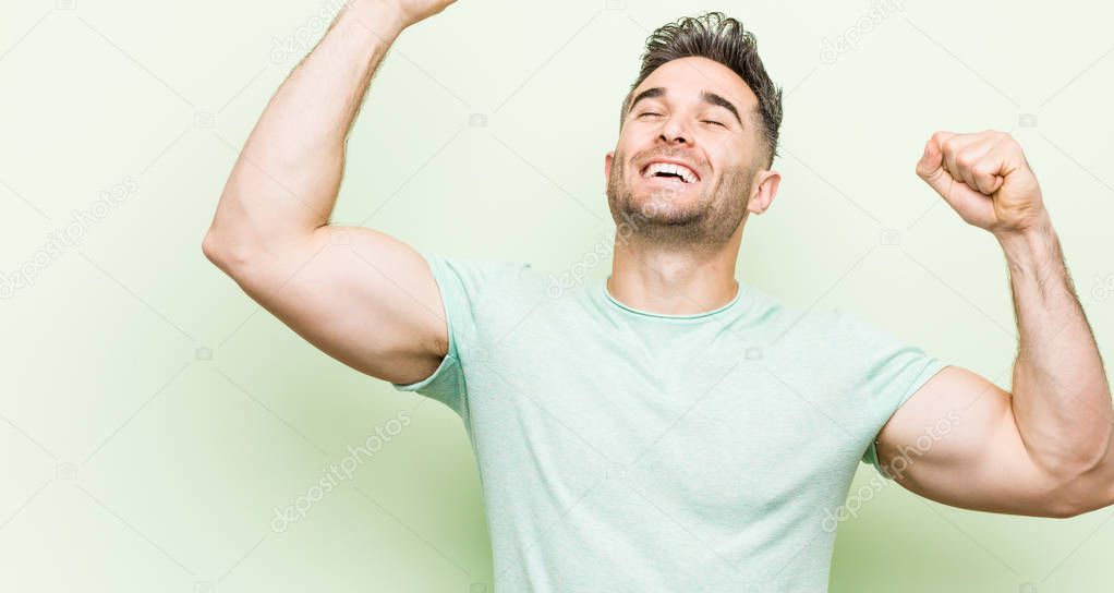 Young handsome man against a green background celebrating a special day, jumps and raise arms with energy.