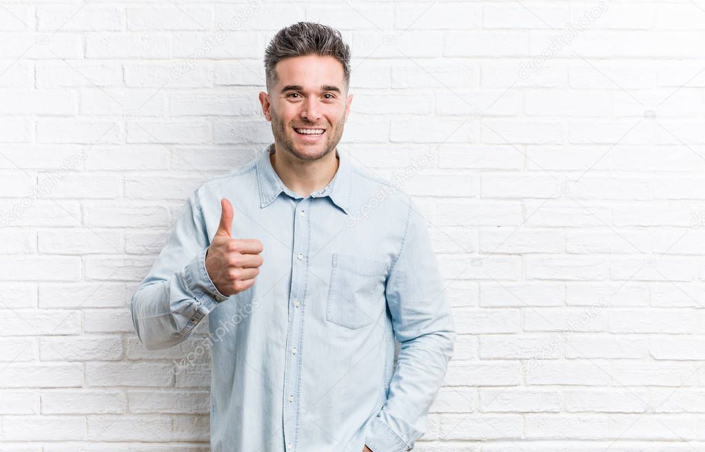 Young handsome man against a bricks wall smiling and raising thumb up