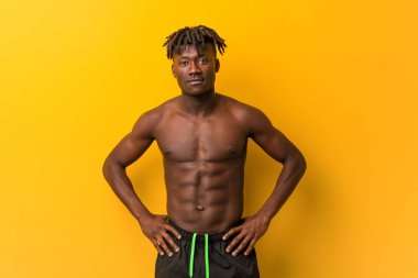 Genç siyah adam mayo giyiyor. Kendine güveniyor. Ellerini kalçasından ayırmıyor..