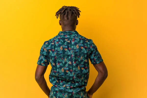 Young black rasta man wearing a vacation look from behind, looking back.