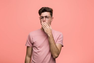 Genç, havalı, beyaz bir adam esniyor. Yorgun bir jest yapıyor. Ağzını eliyle kapatıyor..