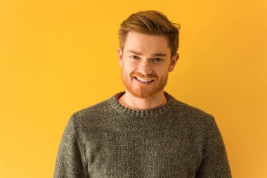 Genç, kızıl saçlı, yakından bakan, neşeli, büyük bir gülümsemesi olan bir adam.