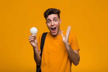 Elinde ampul tutan genç bir öğrenci mutlu, güler yüzlü ve neşeli..