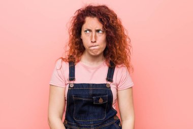 Kot pantolon giyen kızıl saçlı, genç ve güzel bir kadın kafası karışmış, kararsız ve kendinden emin değil..