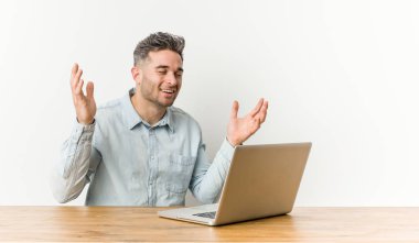 Genç ve yakışıklı bir adam dizüstü bilgisayarıyla çok gülerek çalışıyor. Mutluluk kavramı.