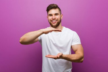 Genç yakışıklı beyaz adam iki eliyle bir şey tutan, ürün sunumu.
