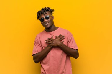 Güneş gözlüğü takan genç siyahi bir adam, dostane bir ifadeye sahiptir, avuçlarını göğsüne bastırır. Aşk konsepti.