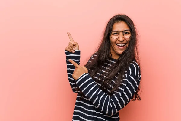 Young intellectual indian woman pointing with forefingers to a copy space, expressing excitement and desire.