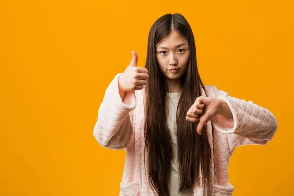 Mladá Číňanka Pyžamu Ukazující Palce Nahoru Palce Dolů Obtížné Vybrat — Stock fotografie