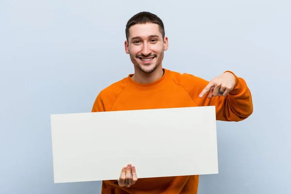 Young Caucasian Man Holding Placard Smiling Cheerfully Pointing Forefinger Away — ストック写真