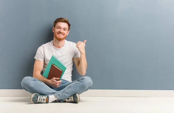 Young Redhead Student Man Sitting Floor Pointing Side Finger Holding — Stock Photo, Image