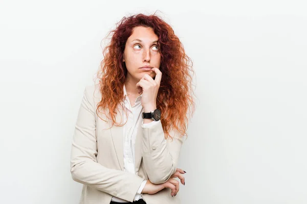 Young natural redhead business woman isolated against white background looking sideways with doubtful and skeptical expression.