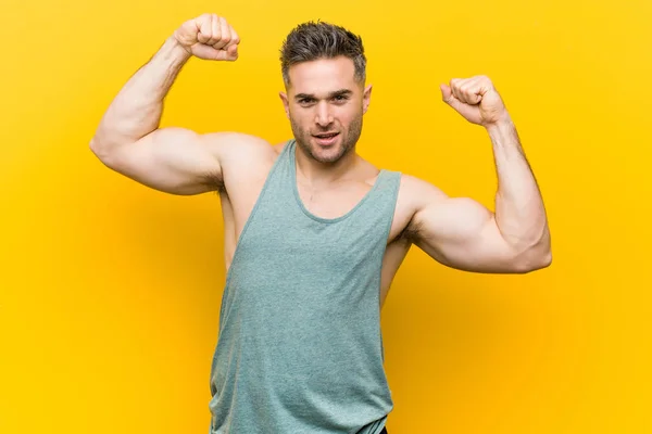 Young fitness man against a yellow background showing strength gesture with arms, symbol of feminine power