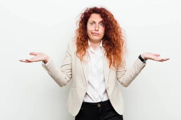Young natural redhead business woman isolated against white background doubting and shrugging shoulders in questioning gesture.