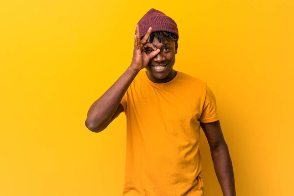 Young black man wearing rastas over yellow background excited keeping ok gesture on eye.