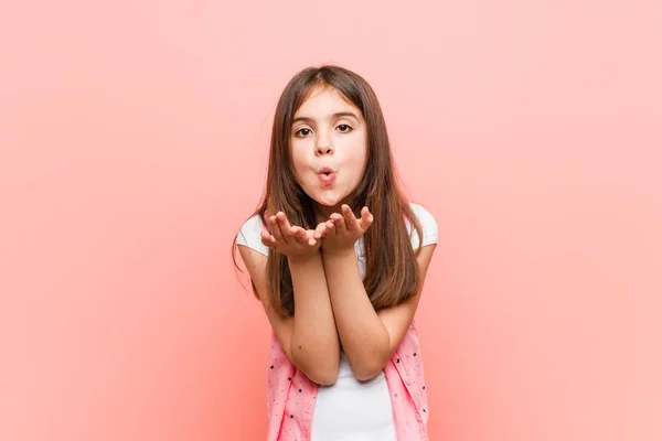 Cute little girl folding lips and holding palms to send air kiss.