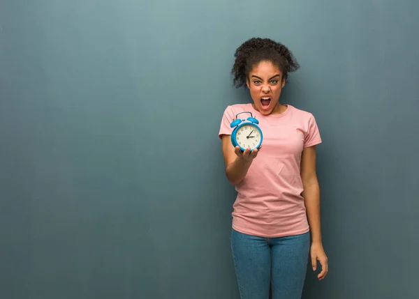 Young black woman screaming very angry and aggressive. She is holding an alarm clock.