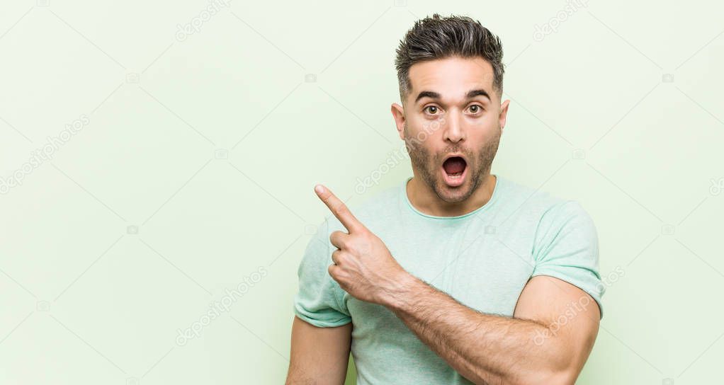 Young handsome man against a green background pointing to the side