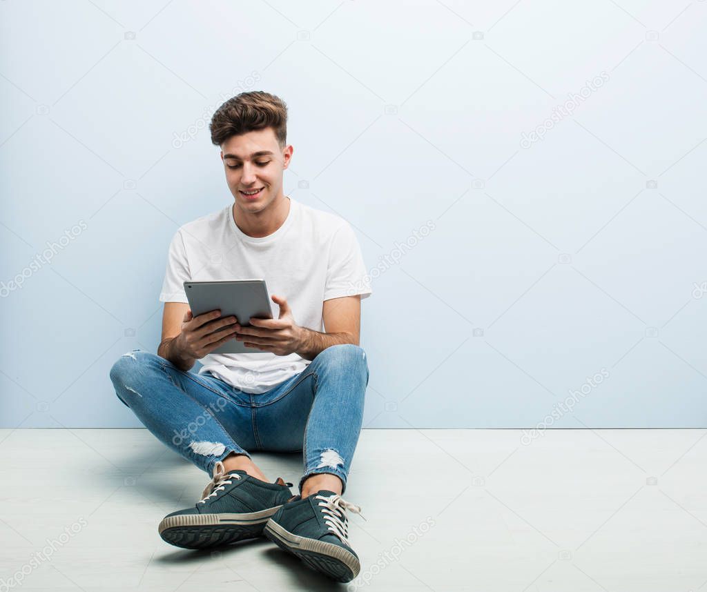 Young man holding a tablet sitting indoor happy, smiling and cheerful.