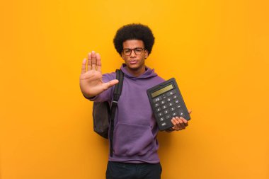 Genç Afrikalı Amerikalı öğrenci elinde hesap makinesiyle elini öne koyuyor.