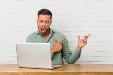 Genç Filipinli adam dizüstü bilgisayarıyla oturup işaret parmağıyla fotokopi alanını işaret ederek heyecan ve arzusunu ifade ediyor..