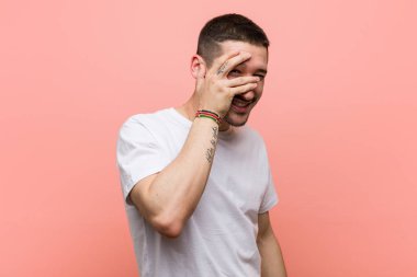 Genç adam kameraya parmaklarıyla göz kırpıyor, utanarak yüzünü kapatıyor..