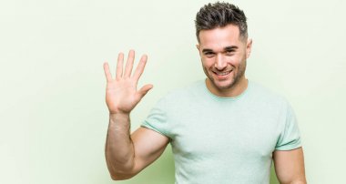 Yeşil bir geçmişi olan genç ve yakışıklı bir adam gülümseyerek beş numarayı parmaklarıyla gösteriyor..