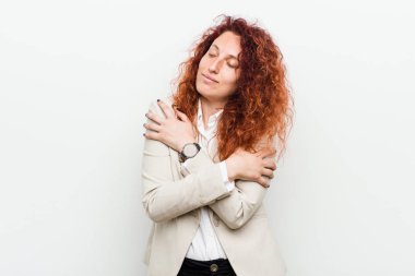 Genç kızıl saçlı iş kadını beyaz arka plan kucaklamalarına karşı izole edilmiş, kaygısız ve mutlu bir şekilde gülümsüyor..