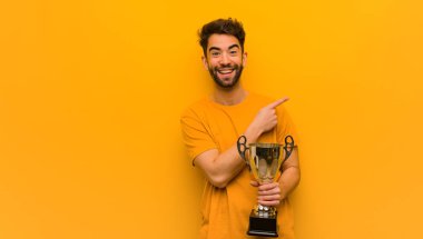 Elinde bir kupa tutan genç adam parmağıyla kenarı işaret ediyor.