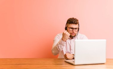 Çağrı merkezinde çalışan genç bir adam kameraya yumruğunu gösteriyor, agresif bir yüz ifadesi..