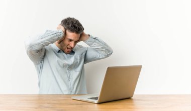 Genç yakışıklı adam laptopuyla çalışıyor kulakları kulaklarıyla tıkayarak yüksek sesli sesler duymamaya çalışıyor..