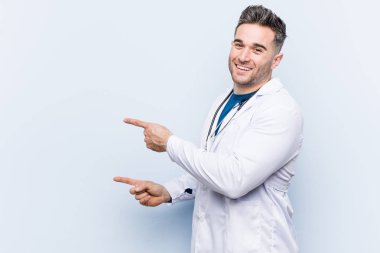 Young handsome doctor man excited pointing with forefingers away. clipart