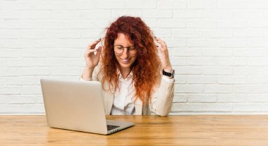 Genç kızıl saçlı kıvırcık kadın laptopuyla çok gülerek çalışıyor. Mutluluk kavramı.