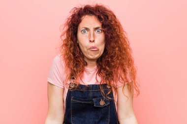 Kot pantolon giyen kızıl saçlı genç bir kadın omuzlarını silker ve kafası karışır..