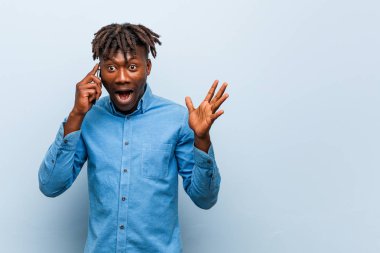 Genç Rasta siyahi adam elinde bir telefonla zaferi ya da başarıyı kutluyor.