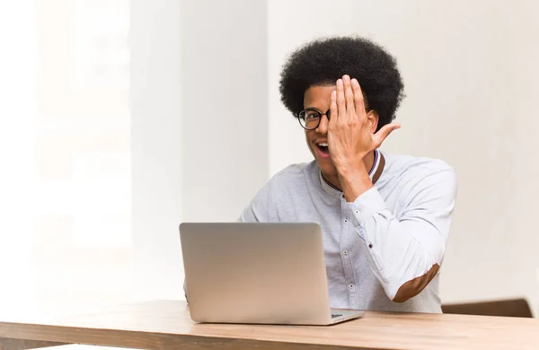 Young black man using his laptop shouting happy and covering face with hand