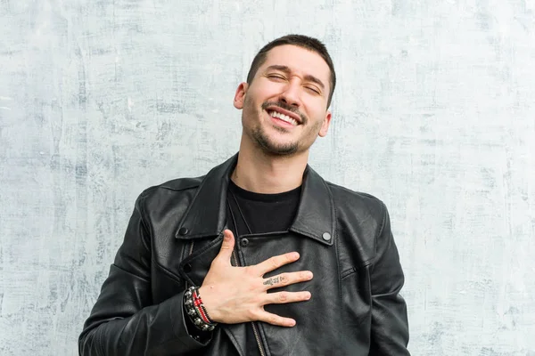 Young rocker man laughs out loudly keeping hand on chest.