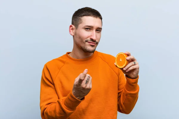 Joven Caucásico Sosteniendo Una Naranja Señalándote Con Dedo Como Invitara — Foto de Stock