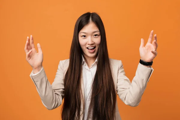 Young business chinese woman receiving a pleasant surprise, excited and raising hands.