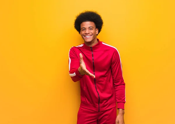 Young sport black man over an orange wall reaching out to greet someone